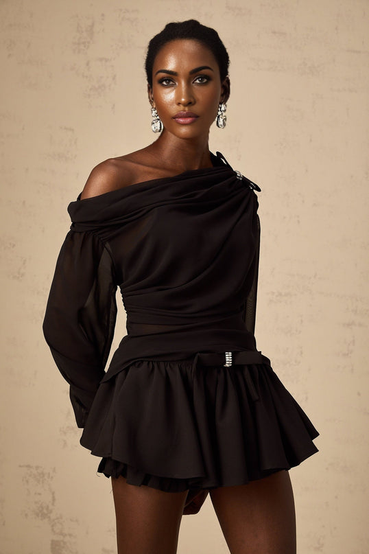 Young woman wearing black asymmetric tulle blouse and matching skirt set from Andrea collection standing against plain background