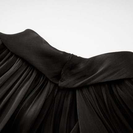 Young woman wearing long black pleated satin maxi dress with flowing skirt and fitted bodice