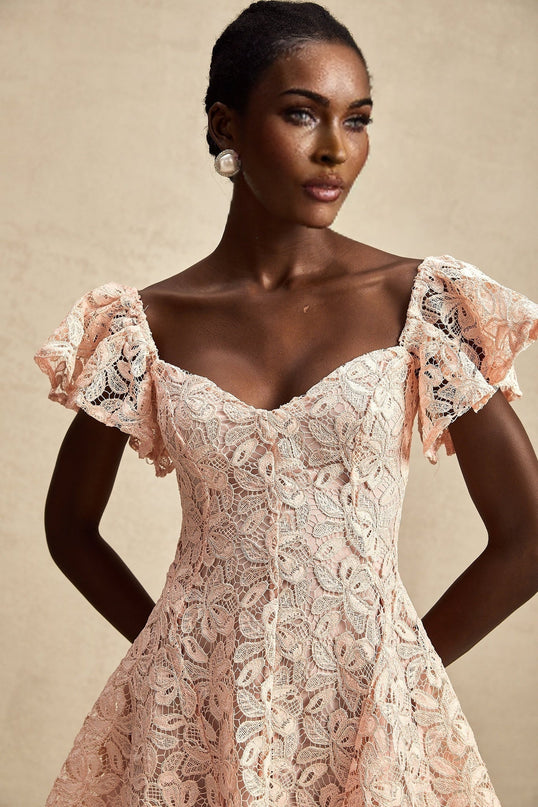 Young woman wearing pink lace mini dress with flutter sleeves standing in outdoor setting