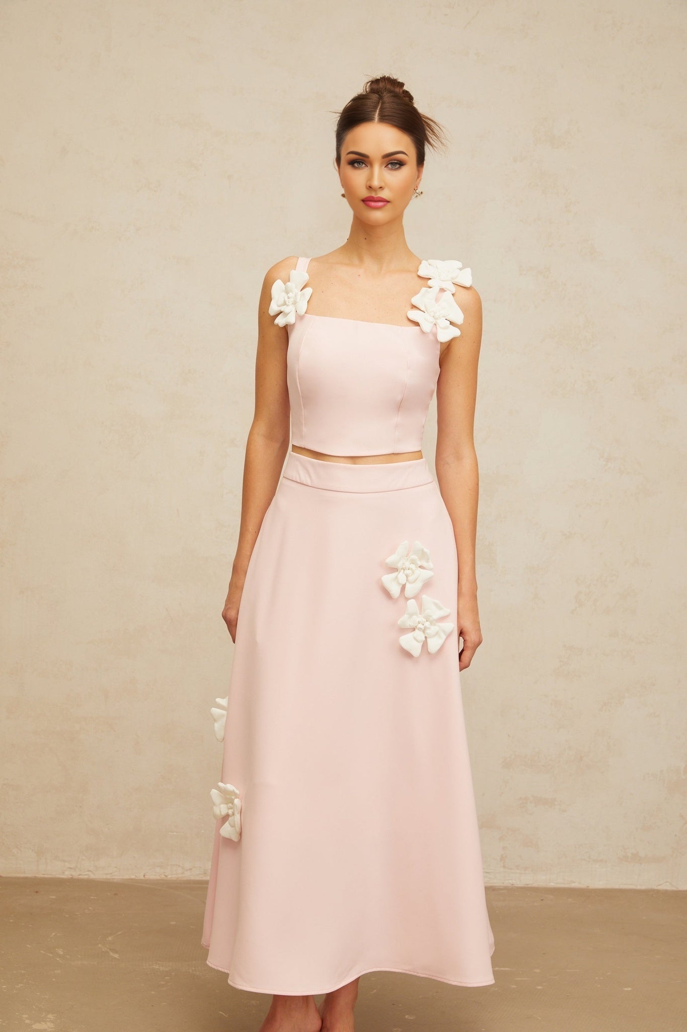 Young woman wearing pink matching set with floral applique top and skirt standing against plain background